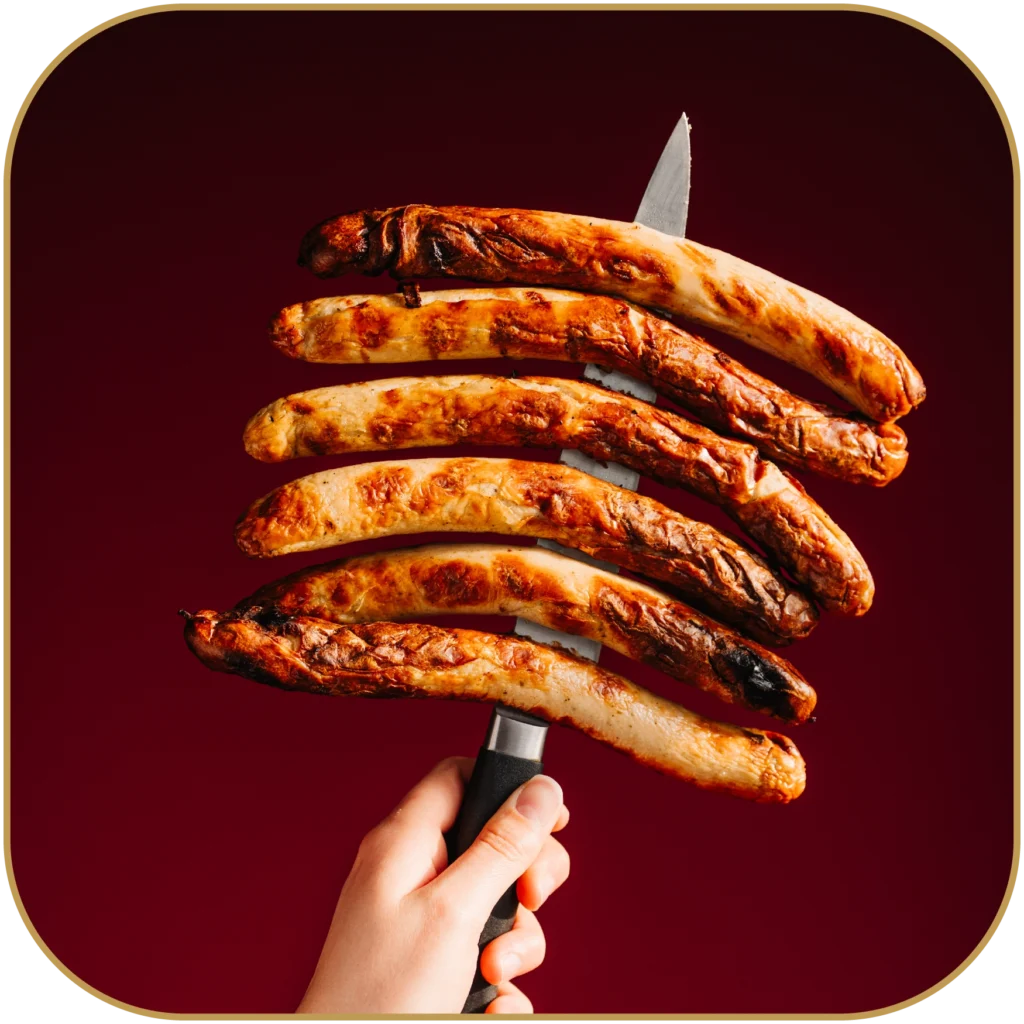 Eine gegrillte Rostbratwurst, auf einem Messer aufgespießt.